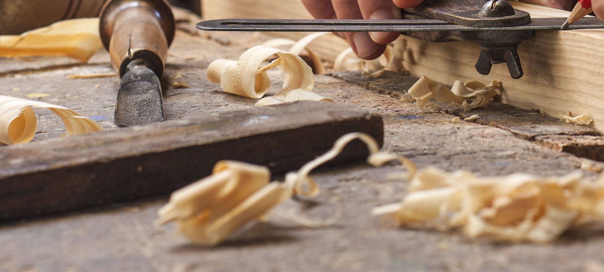 Ein Mitarbeiter schleift Holz sorgfältig mit einem Werkzeug in der Werkstatt
